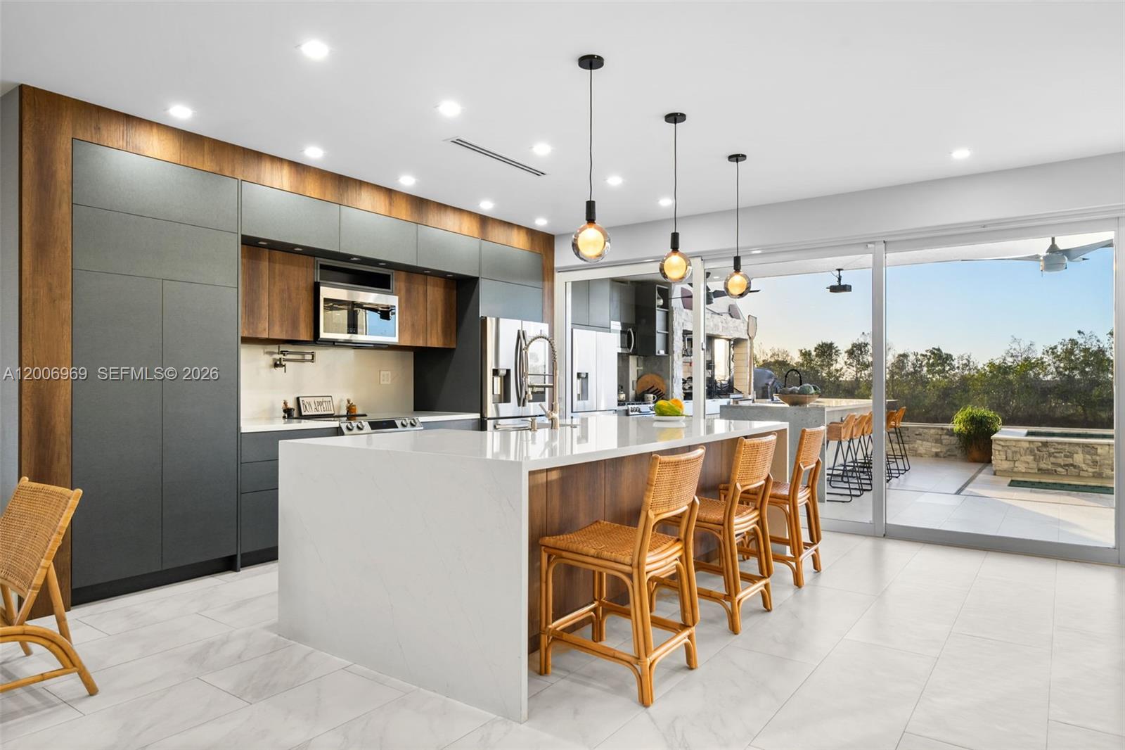 A modern kitchen features a white waterfall island, dark cabinetry, wood accents, and sliding doors — 1828 Aspen Ln, Weston FL 33327, WESTON, FL