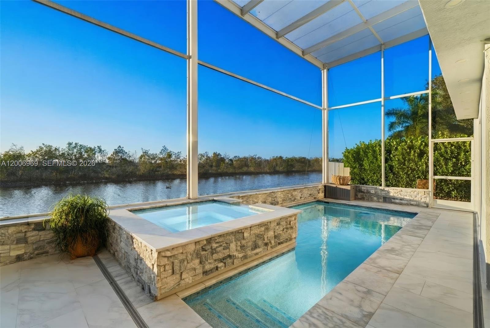 A screened-in patio features a stone-clad hot tub and swimming pool overlooking a canal — 1828 Aspen Ln, Weston FL 33327, WESTON, FL