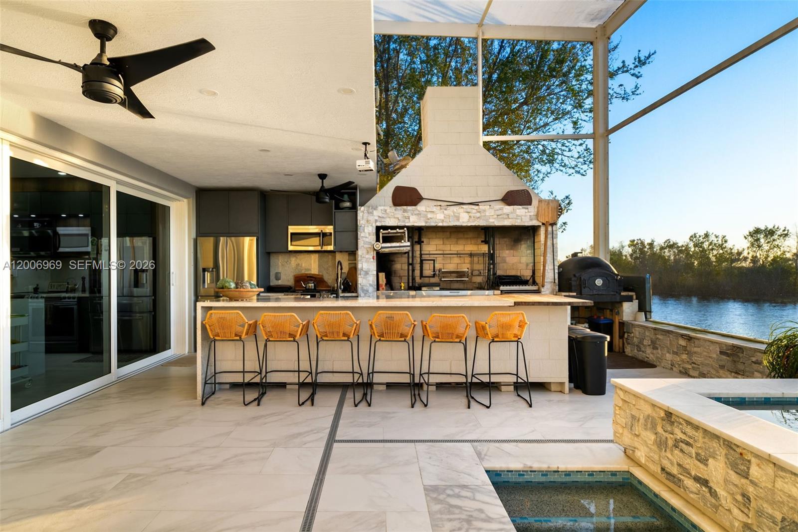 An outdoor kitchen with a grill, bar seating, and a pool overlooks a waterfront view — 1828 Aspen Ln, Weston FL 33327, WESTON, FL