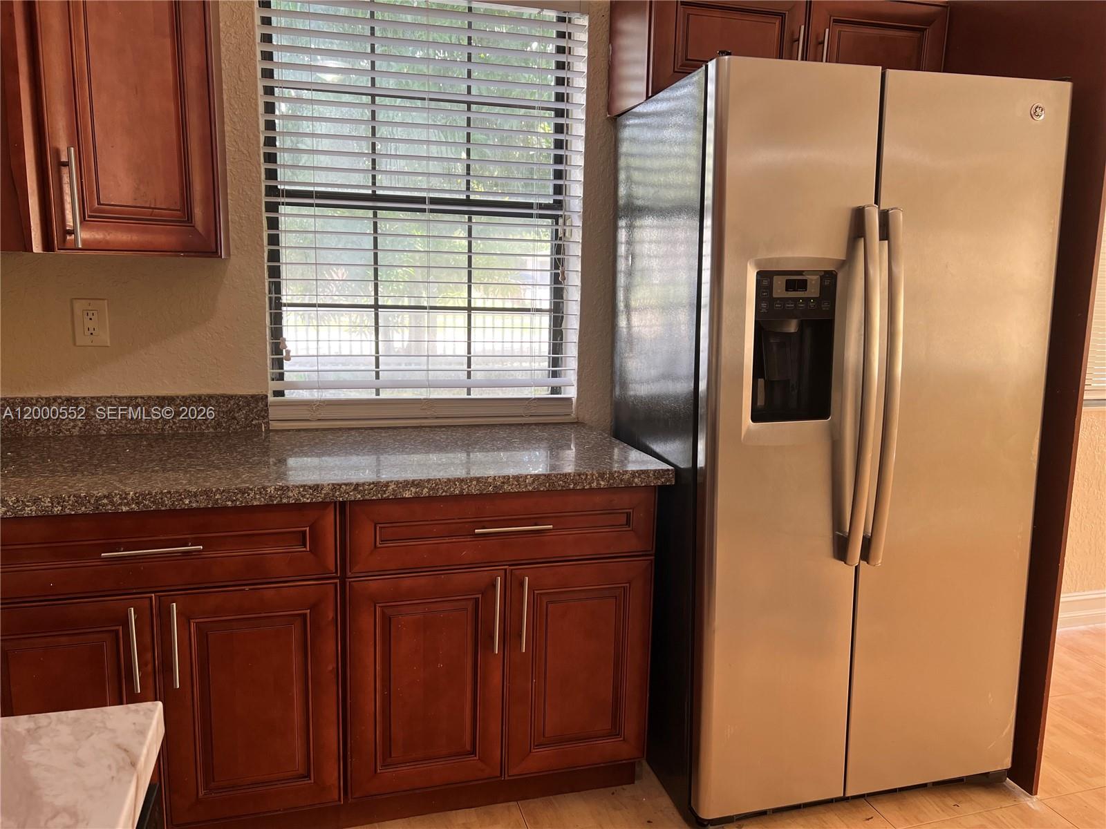 A kitchen features dark wood cabinets, granite countertops, a window with blinds, and a refrigerator — 931 NW 34th Way, Lauderhill FL 33311, LAUDERHILL, FL