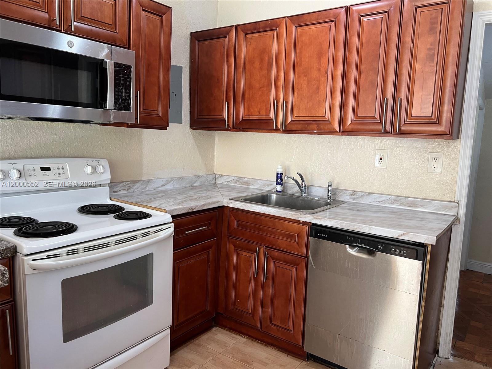 A kitchen features wood cabinets, a white stove, a stainless steel dishwasher, and marble-patterned countertops — 931 NW 34th Way, Lauderhill FL 33311, LAUDERHILL, FL