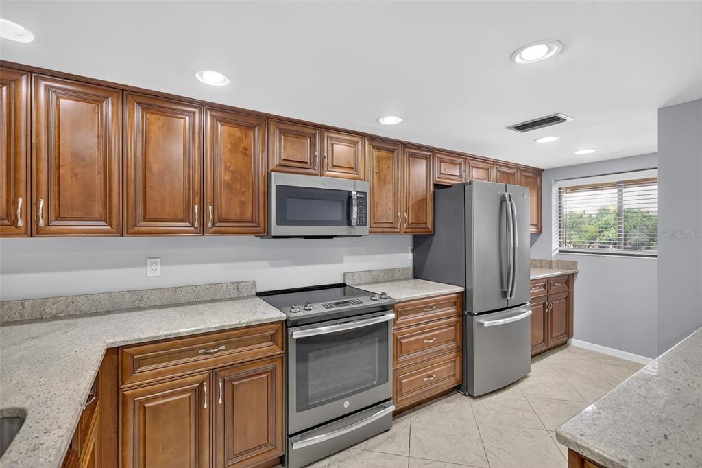 A kitchen features wood cabinets, stainless steel appliances, granite countertops, and tile flooring — 1724 GOLFVIEW DRIVE, TARPON SPRINGS, FL