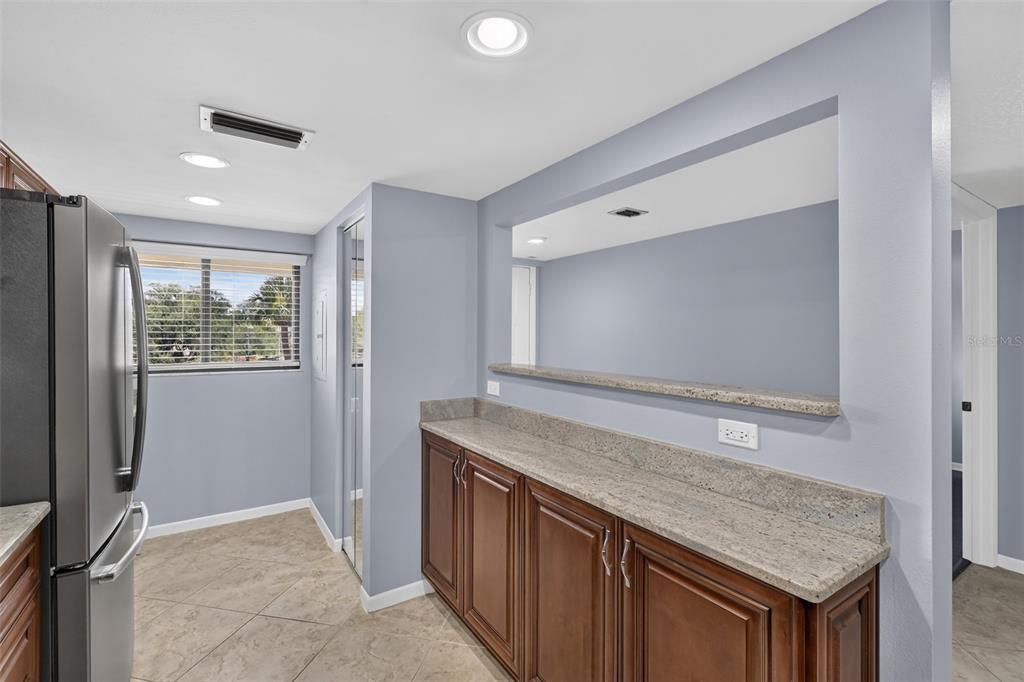 A kitchen features dark wood cabinets, granite countertops, a pass-through window, and tile flooring — 1724 GOLFVIEW DRIVE, TARPON SPRINGS, FL