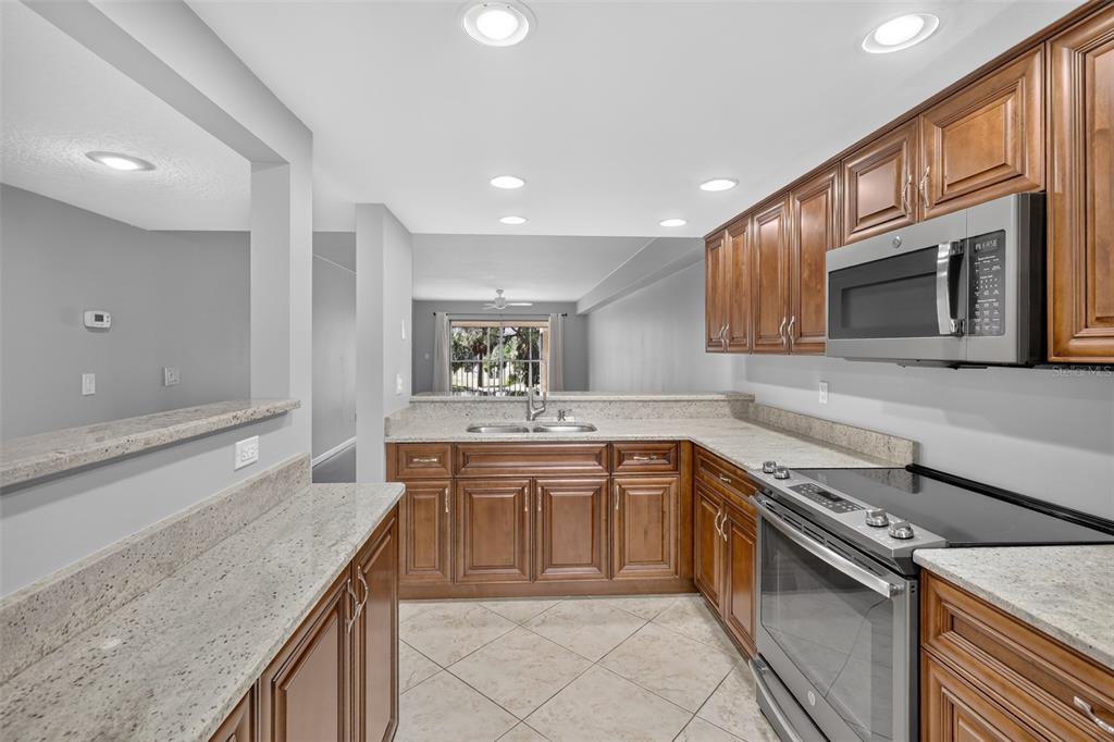 A kitchen features wood cabinets, granite countertops, stainless steel appliances, and tile flooring — 1724 GOLFVIEW DRIVE, TARPON SPRINGS, FL