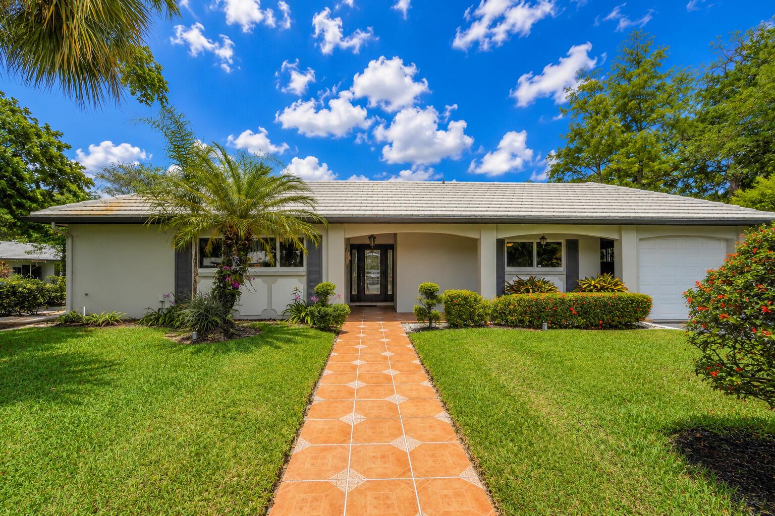 A single-story house with a tiled walkway, palm tree, and green lawn under a blue sky — 1019 E Cypress Drive, Pompano Beach FL 33069, POMPANO BEACH, FL