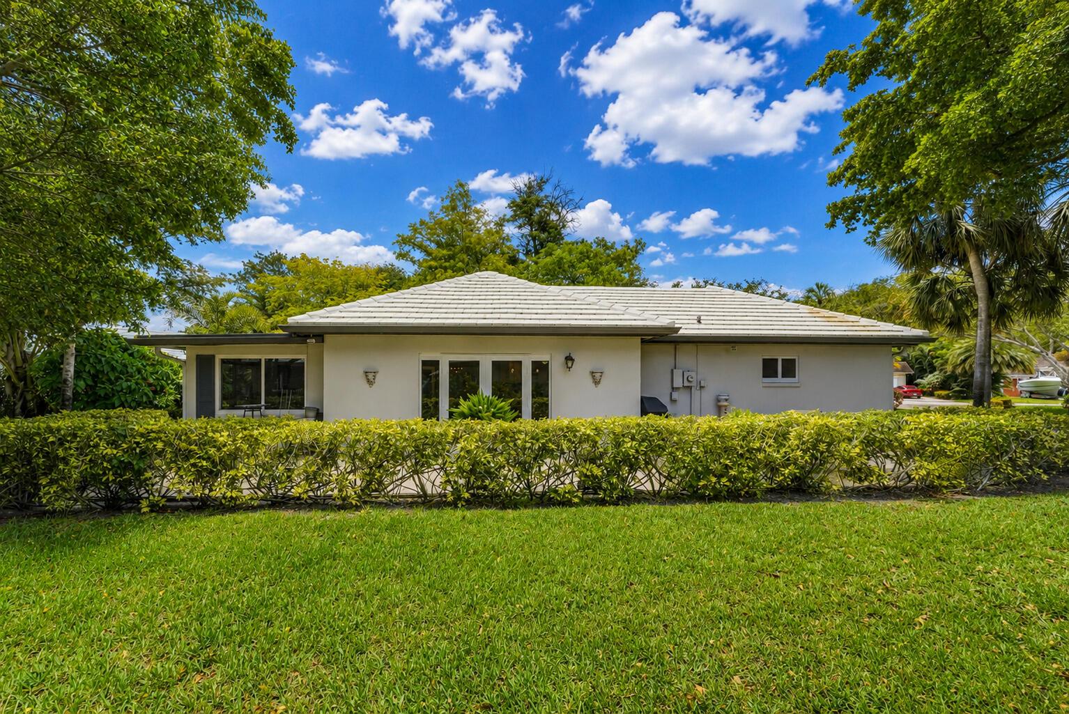 A single-story house with a white tiled roof sits behind a manicured hedge and lawn — 1019 E Cypress Drive, Pompano Beach FL 33069, POMPANO BEACH, FL