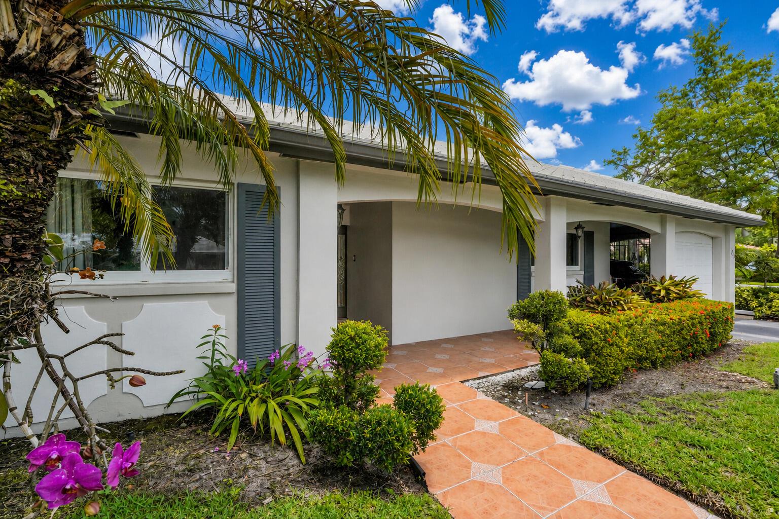 A tiled walkway leads to the covered entrance of a single-story house with gray shutters — 1019 E Cypress Drive, Pompano Beach FL 33069, POMPANO BEACH, FL