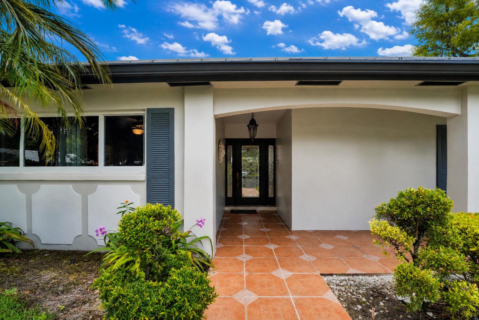 A front entryway with a tiled porch, a dark glass door, and white exterior walls — 1019 E Cypress Drive, Pompano Beach FL 33069, POMPANO BEACH, FL