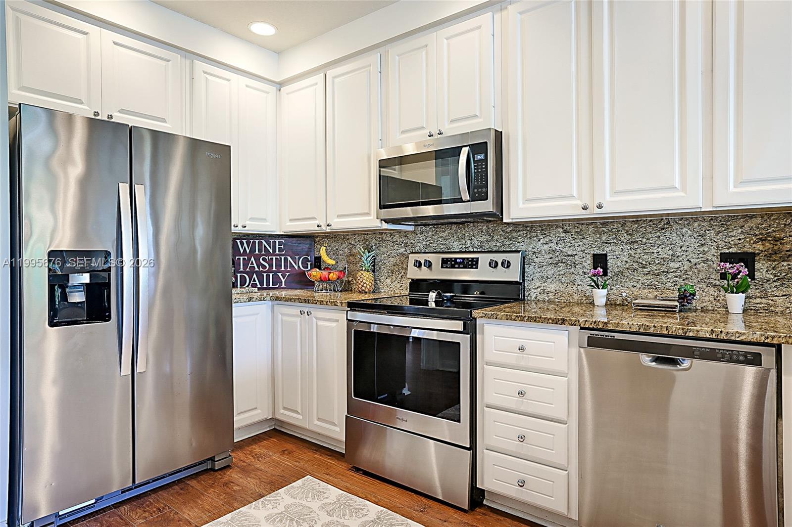A kitchen features white cabinets, stainless steel appliances, and granite countertops over hardwood flooring — 3414 W Mallory Blvd, Jupiter FL 33458, JUPITER, FL