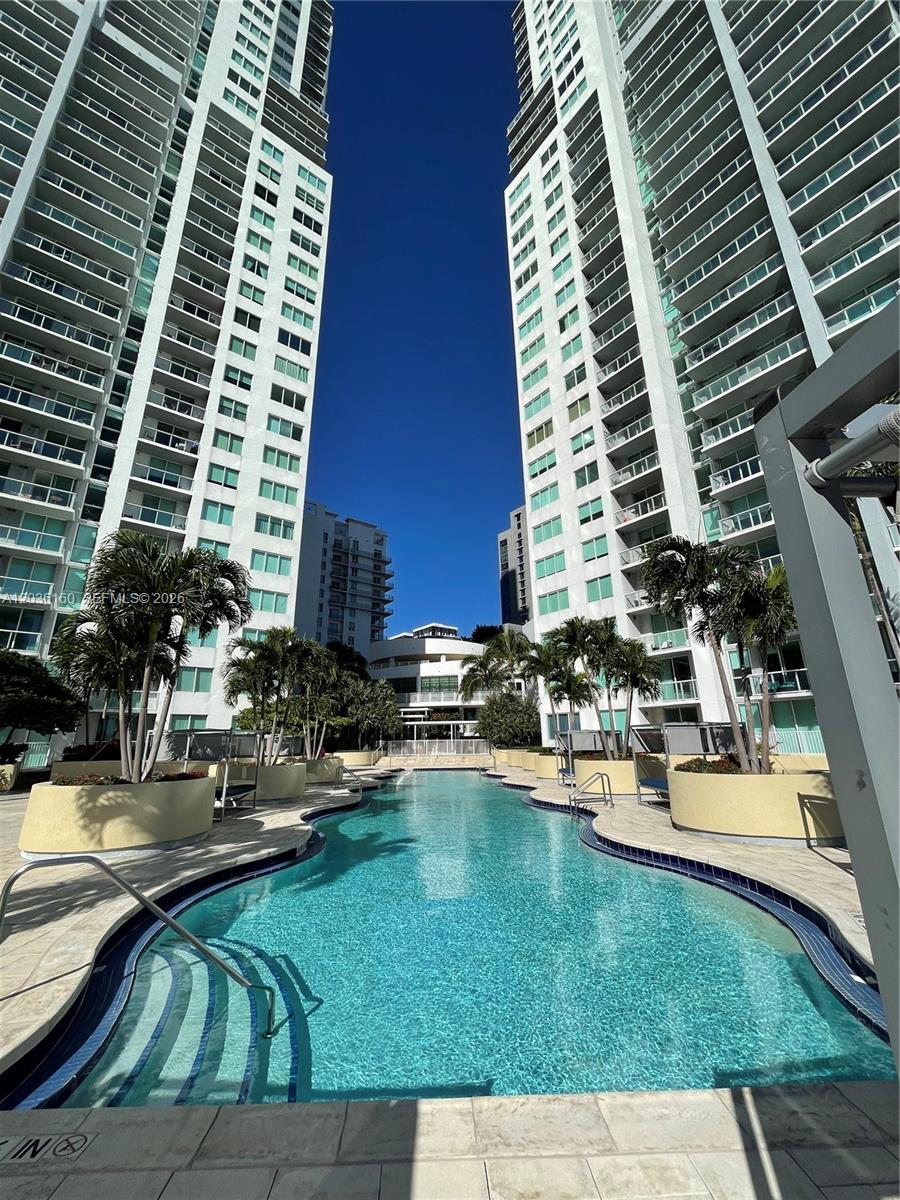 A swimming pool sits between two tall white residential buildings with balconies under a clear sky — 253 NE 2nd St # 2108, Miami FL 33132, MIAMI, FL