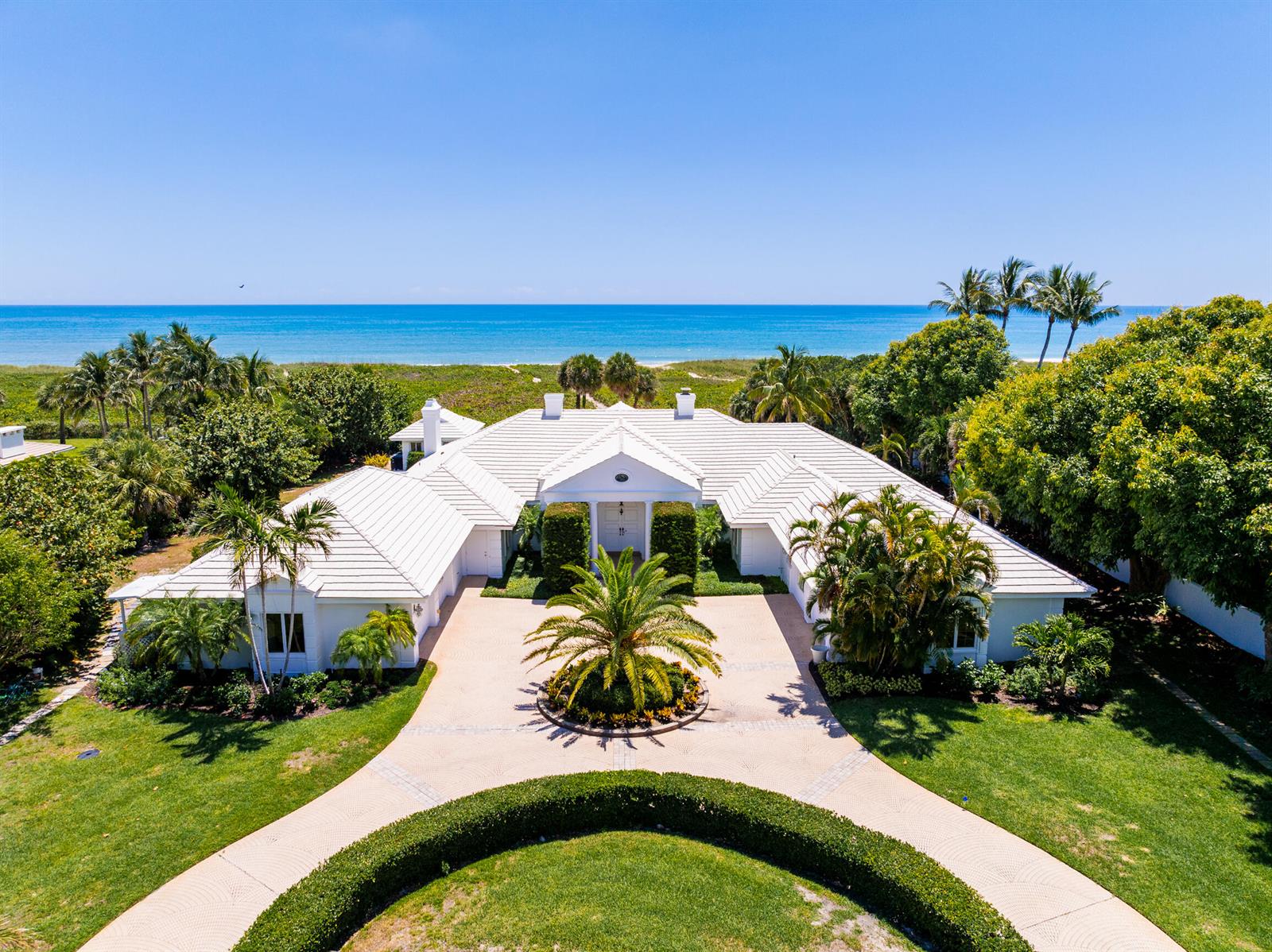 An aerial view of a white, single-story coastal house with a circular driveway and palm trees — VERO BEACH, FL
