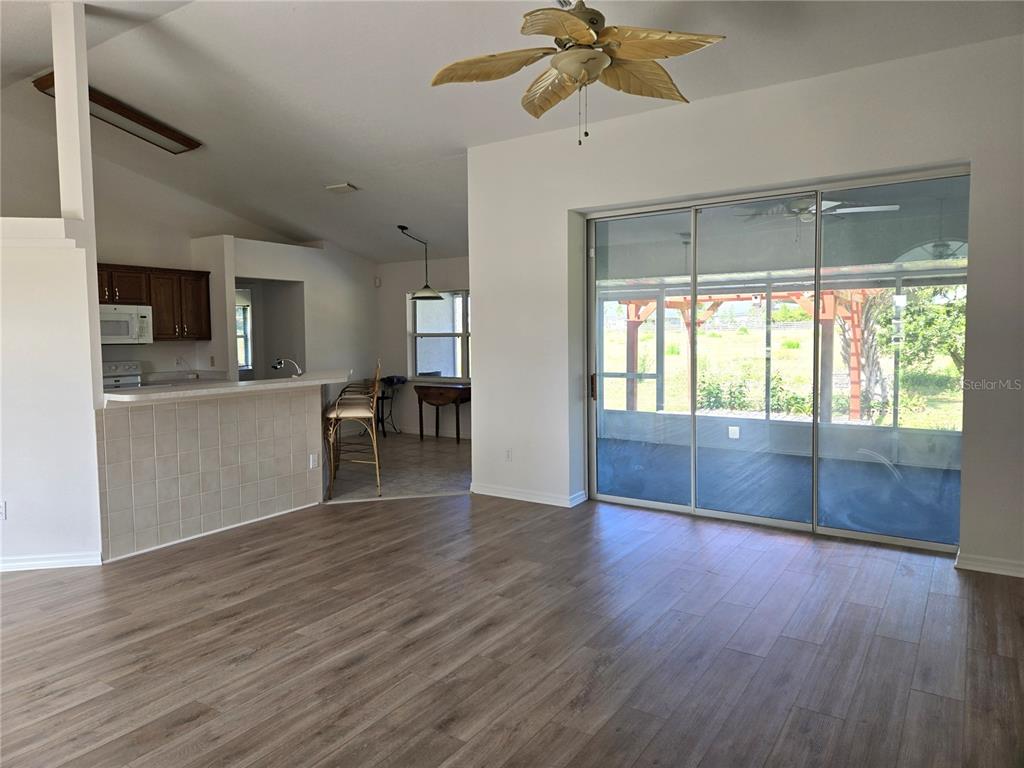 A living room with wood-look flooring leads to a kitchen with a tiled breakfast bar — 3434 NW 50TH COURT, OCALA, FL