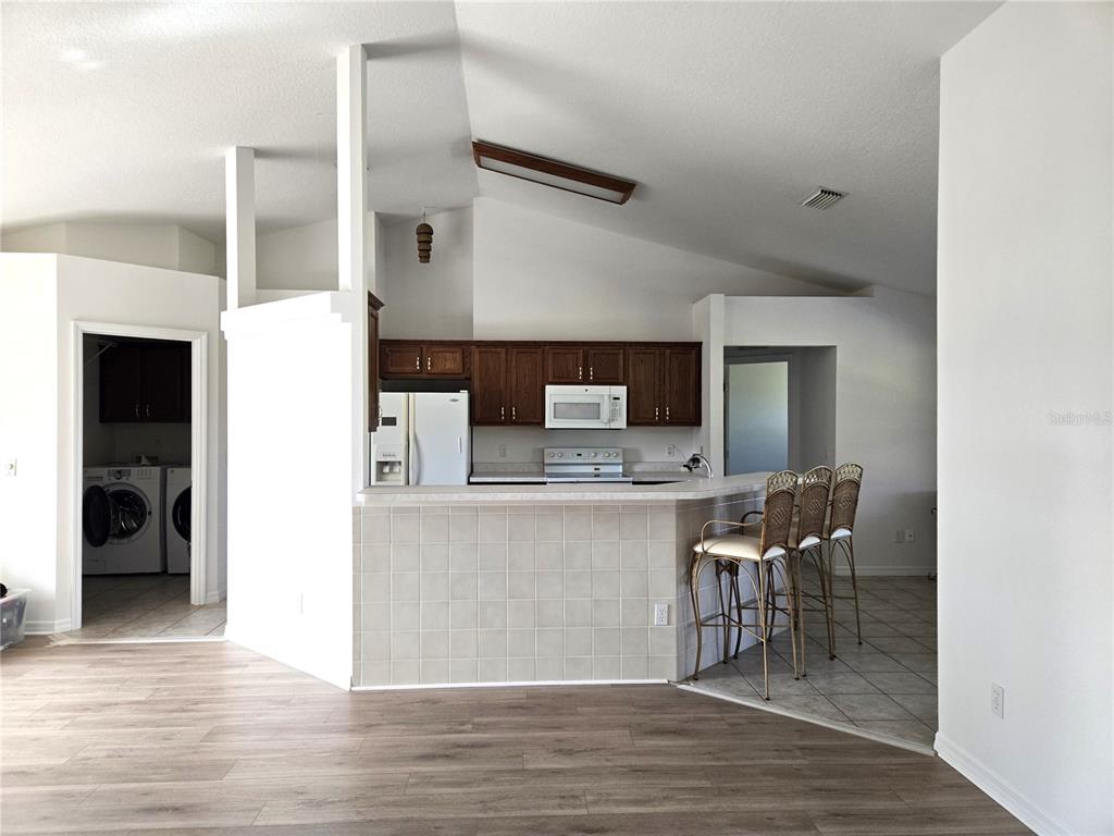 A kitchen with dark wood cabinets and a tiled breakfast bar overlooks a living area — 3434 NW 50TH COURT, OCALA, FL