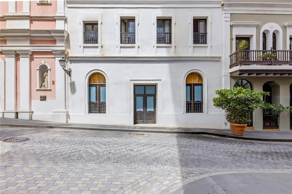 A white building with arched windows and a central doorway stands on a cobblestone street — 205 TETUAN STREET, SAN JUAN, PR