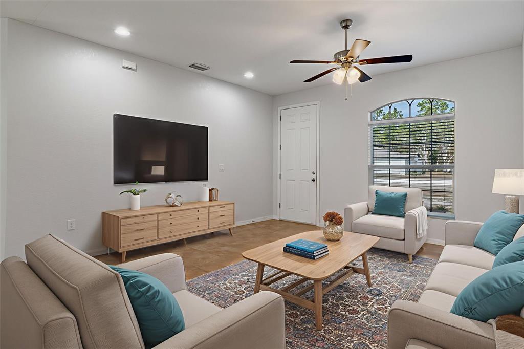 A living room features a wall-mounted television, light wood media console, and neutral seating furniture — 13124 SNOWY PLOVER AVENUE, WEEKI WACHEE, FL