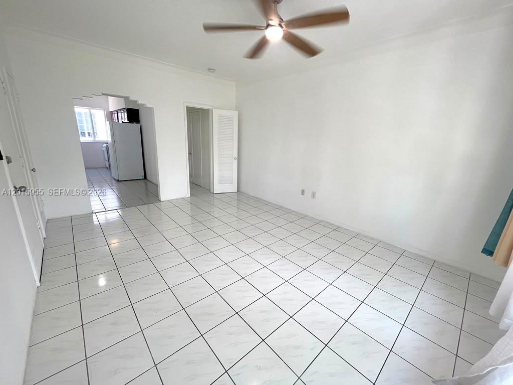 An empty room with white tile floors, a ceiling fan, and an adjacent kitchen area — MIAMI BEACH, FL