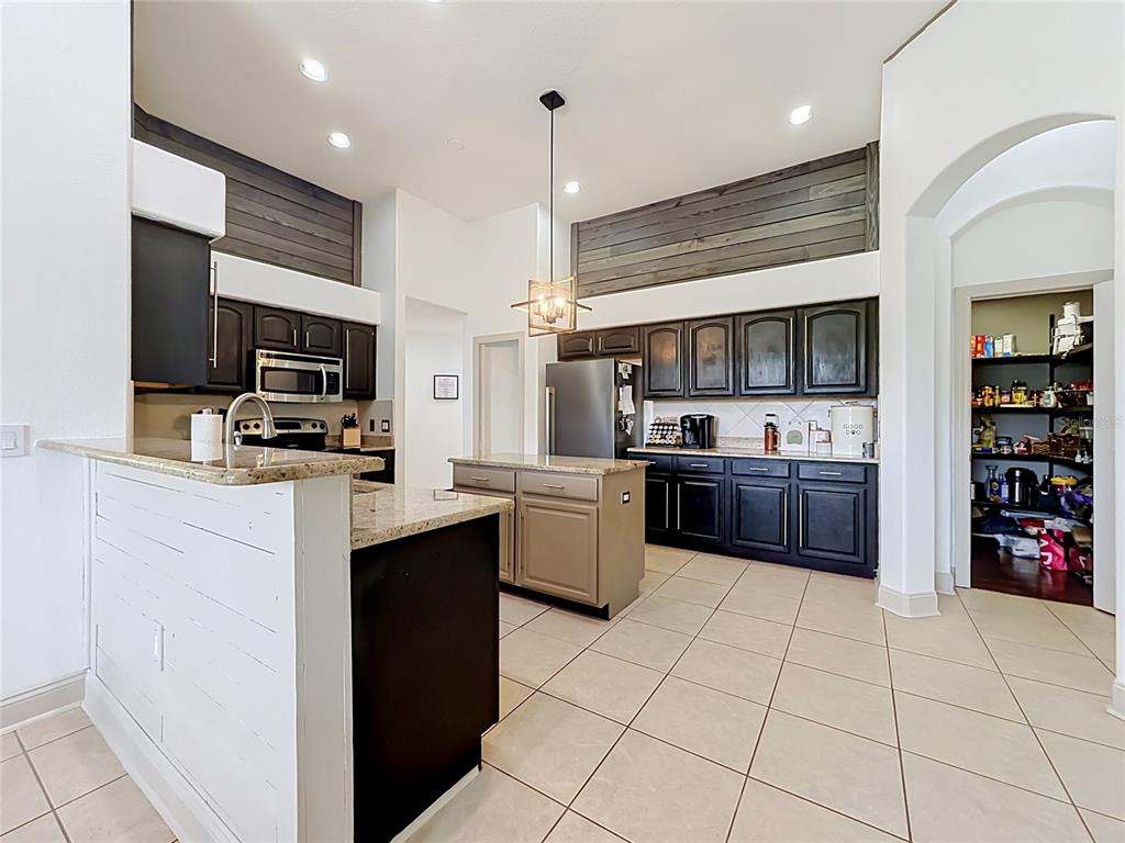 A kitchen features dark cabinetry, a light-colored island, granite countertops, and wood-plank accent walls — 5846 BENT GRASS DRIVE, VALRICO, FL