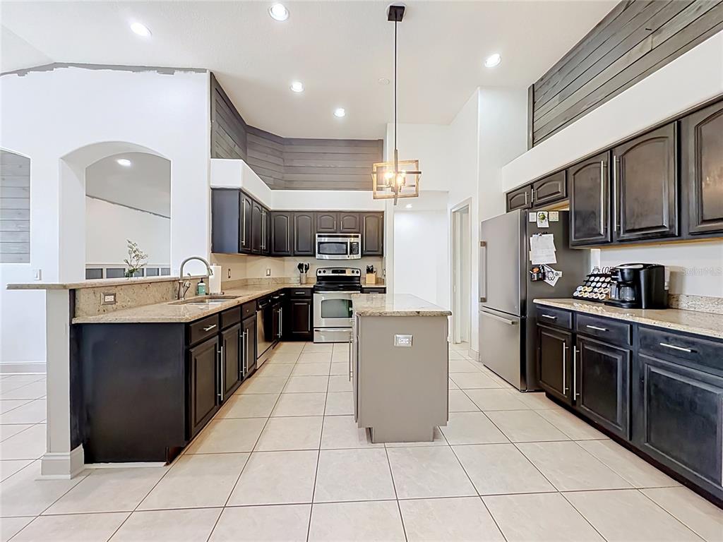 A kitchen features dark cabinets, granite countertops, a central island, and light-colored tile flooring — 5846 BENT GRASS DRIVE, VALRICO, FL