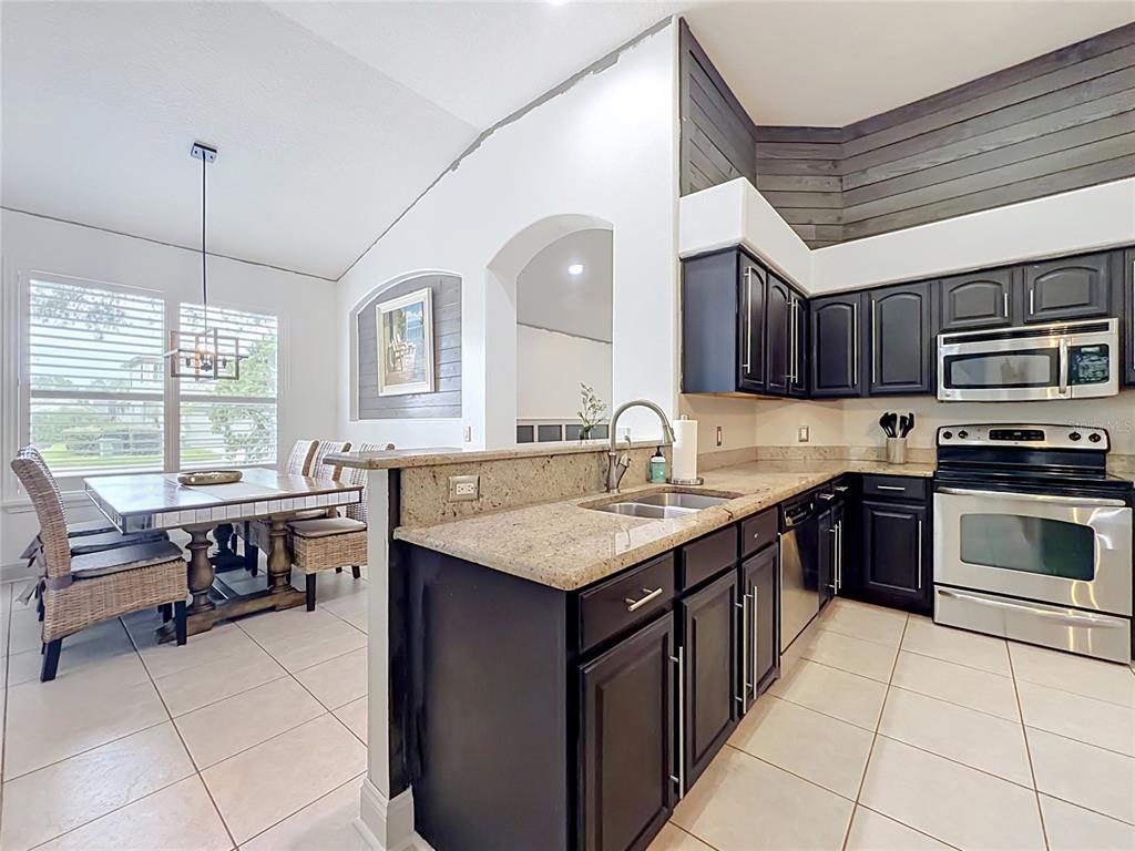 A kitchen with dark cabinets and granite countertops overlooks a dining area with tile floors — 5846 BENT GRASS DRIVE, VALRICO, FL