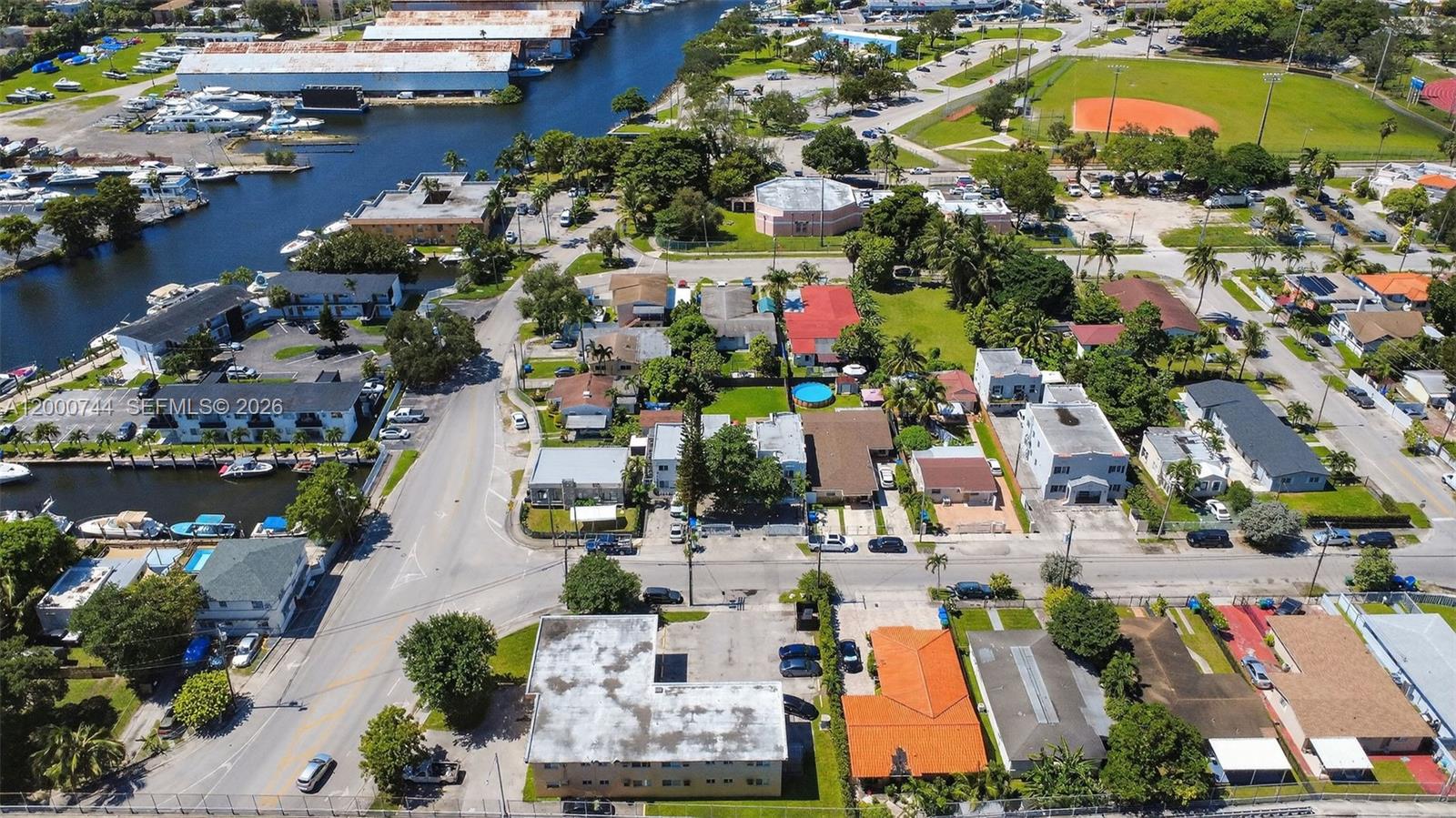 An aerial view shows a neighborhood with houses, apartment buildings, a canal, and a baseball field — 1680 NW 22nd Ct, Miami FL 33125, MIAMI, FL