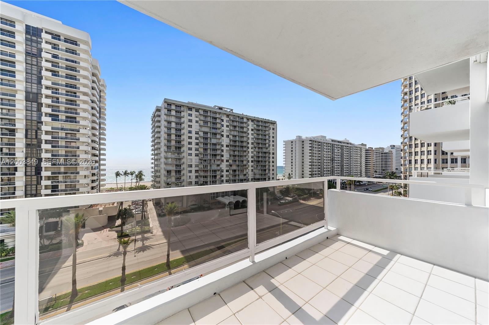 A high-rise balcony with white tile flooring overlooks a street, nearby buildings, and the ocean — 5700 Collins Ave # 8A, Miami Beach FL 33140, MIAMI BEACH, FL