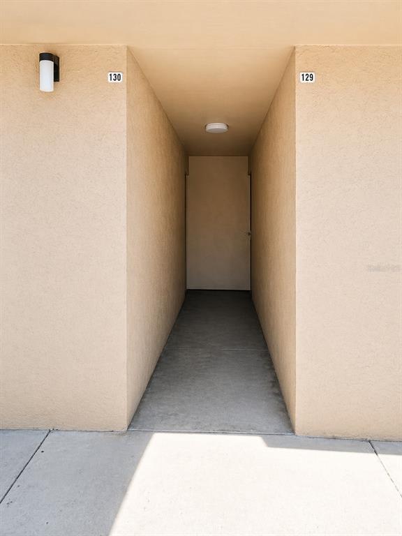 A narrow outdoor walkway leads to a single door between two beige apartment units — 5820 N CHURCH AVENUE UNIT 129, TAMPA, FL