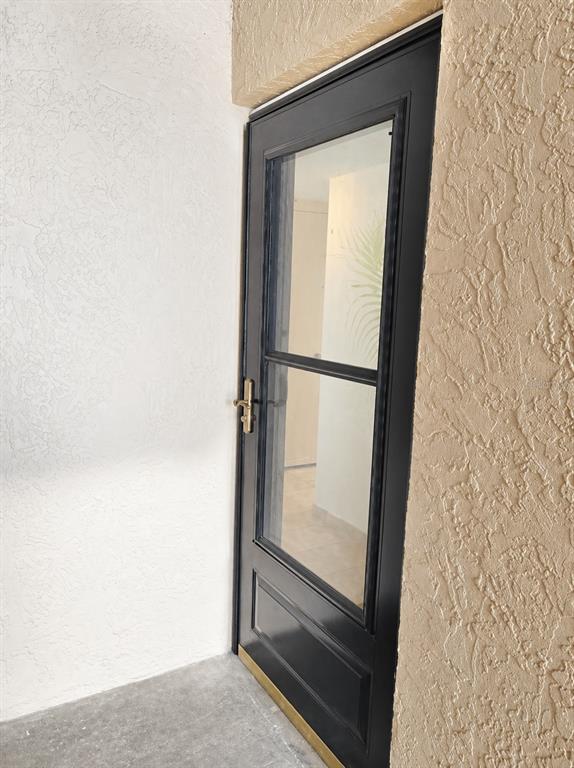 A black storm door with a glass panel is installed in a textured stucco entryway — 5820 N CHURCH AVENUE UNIT 129, TAMPA, FL