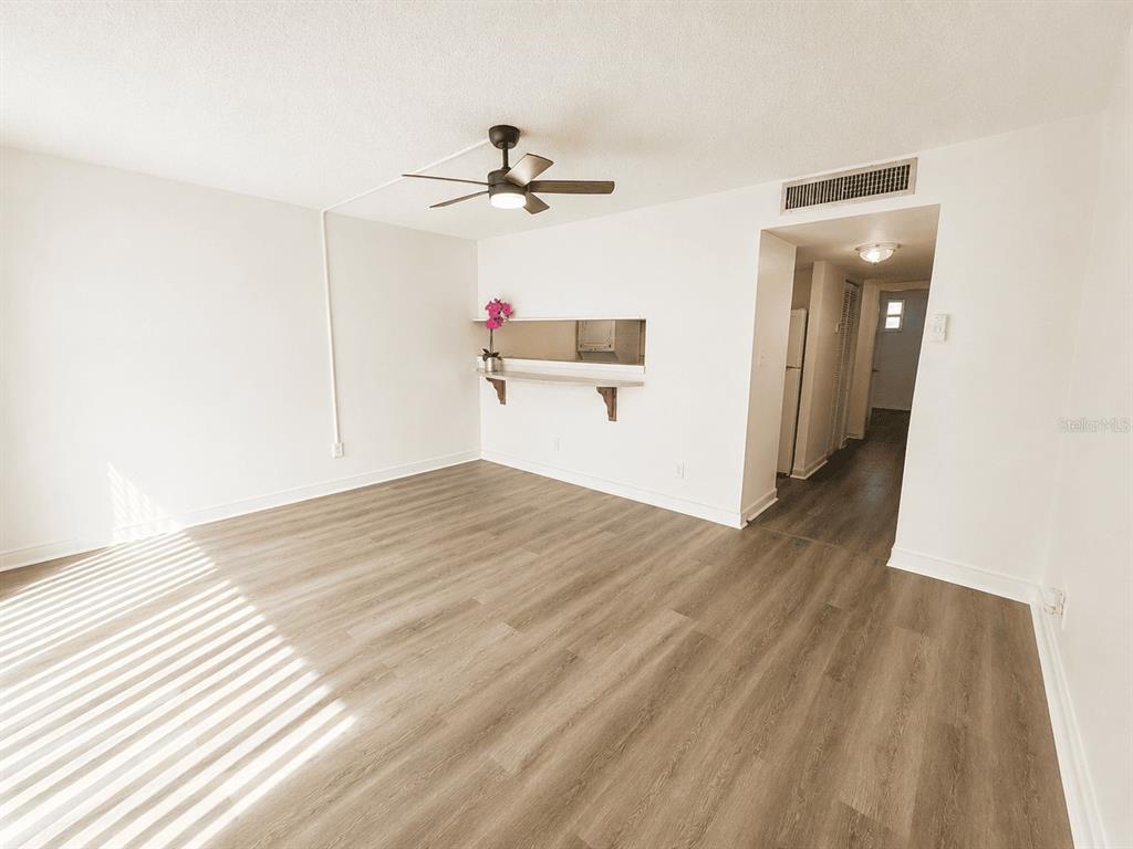 An empty living room features light wood-look flooring, a ceiling fan, and a kitchen pass-through — 5820 N CHURCH AVENUE UNIT 129, TAMPA, FL
