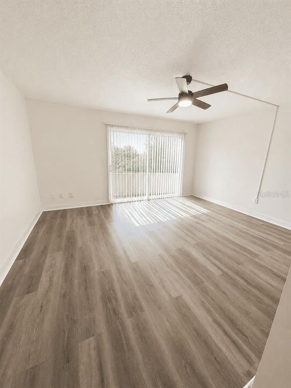 An empty room with light wood-look flooring, a ceiling fan, and sliding glass balcony doors — 5820 N CHURCH AVENUE UNIT 129, TAMPA, FL