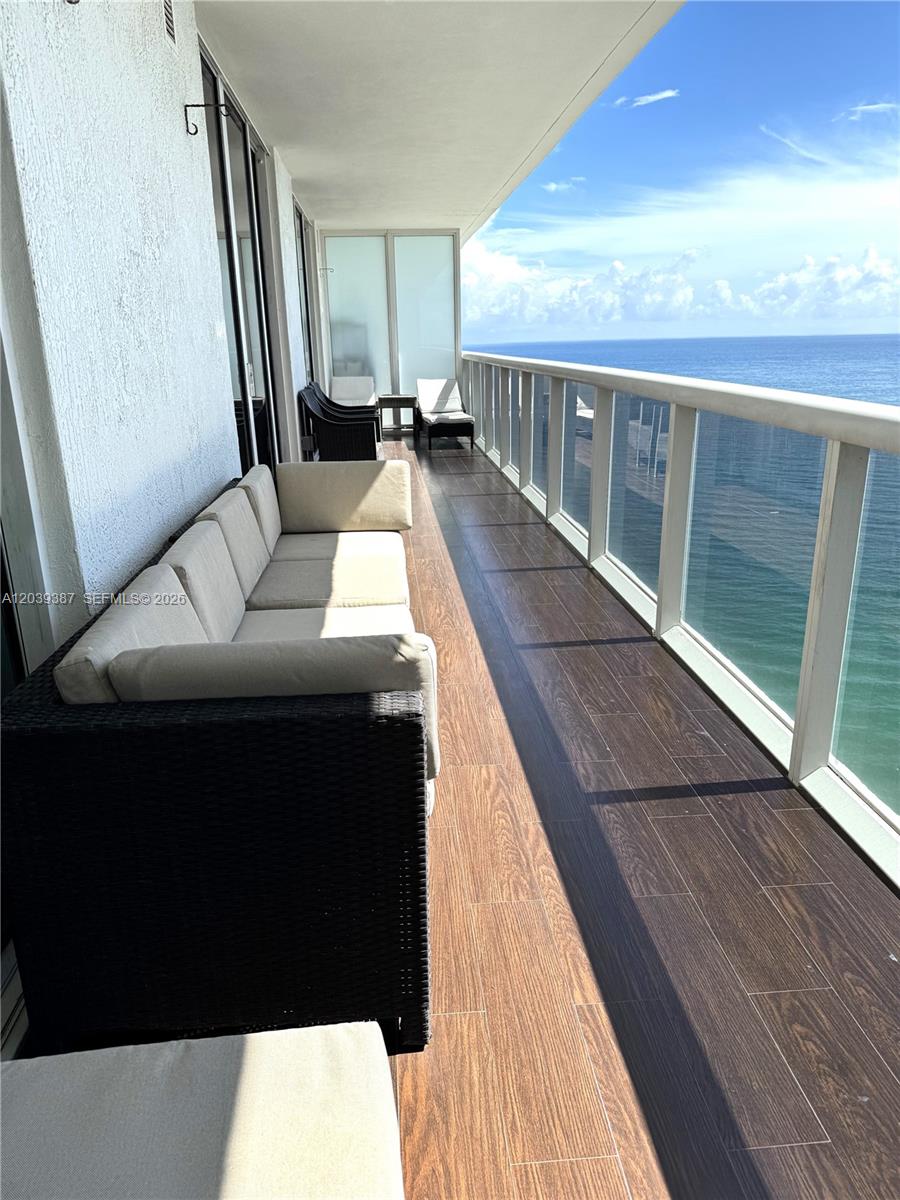 A long balcony features wood-look tile flooring, outdoor seating, and a glass railing overlooking the ocean — 1830 S Ocean Dr # 3303, Hallandale Beach FL 33009, HALLANDALE BEACH, FL
