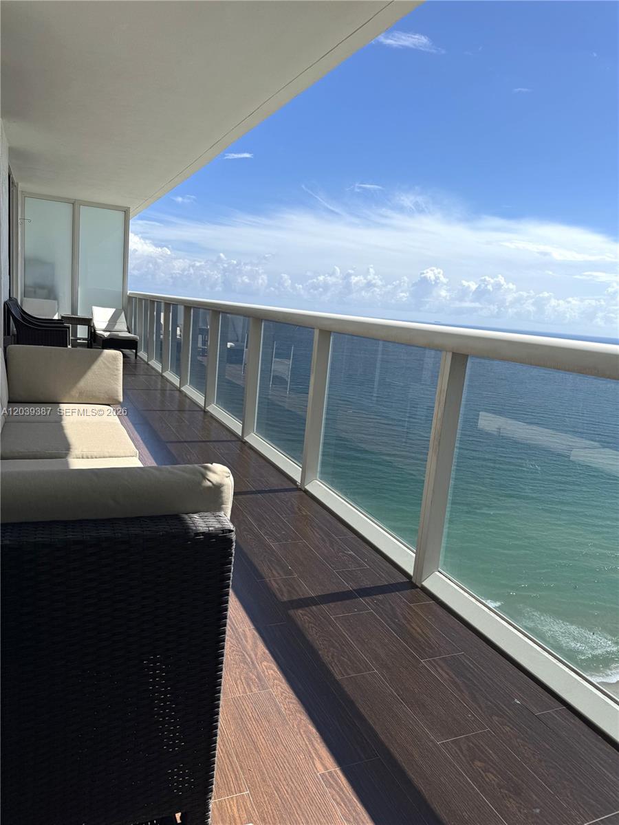 A balcony with dark wood-look tile flooring features outdoor furniture overlooking the ocean — 1830 S Ocean Dr # 3303, Hallandale Beach FL 33009, HALLANDALE BEACH, FL