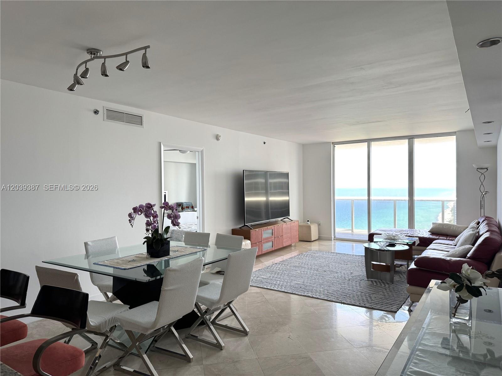 A modern living and dining area features a glass table, white chairs, and ocean views — 1830 S Ocean Dr # 3303, Hallandale Beach FL 33009, HALLANDALE BEACH, FL