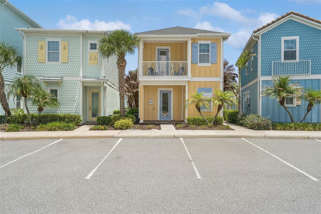 A yellow two-story house sits between two other colorful homes with a parking lot foreground — 8081 KNEE DEEP ROAD, KISSIMMEE, FL