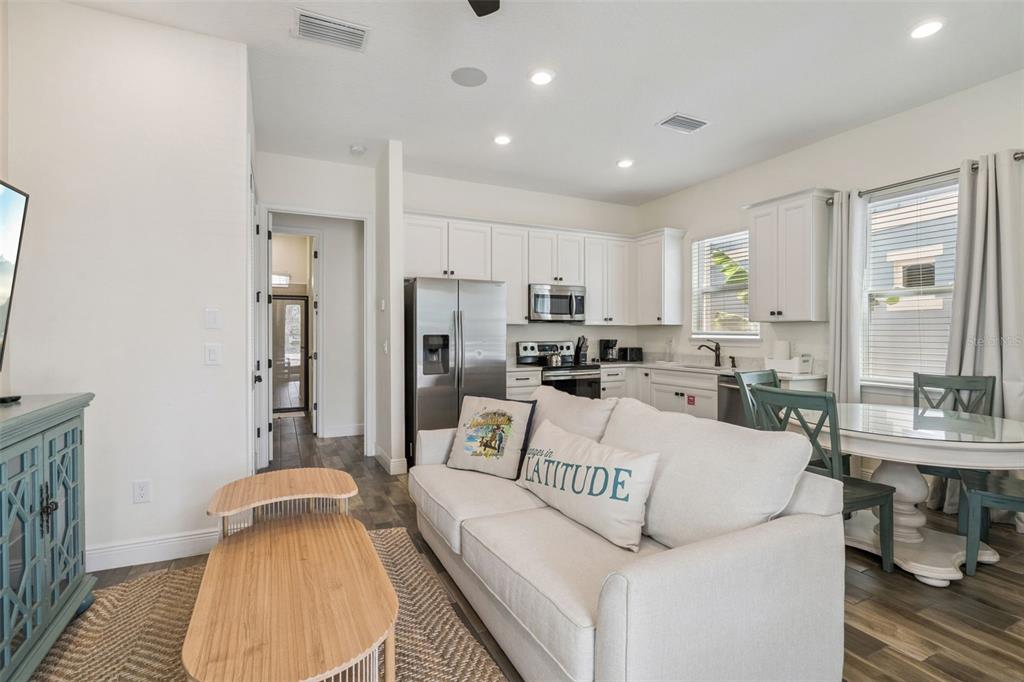 An open-concept living room and kitchen featuring white cabinetry, stainless steel appliances, and light furniture — 8081 KNEE DEEP ROAD, KISSIMMEE, FL