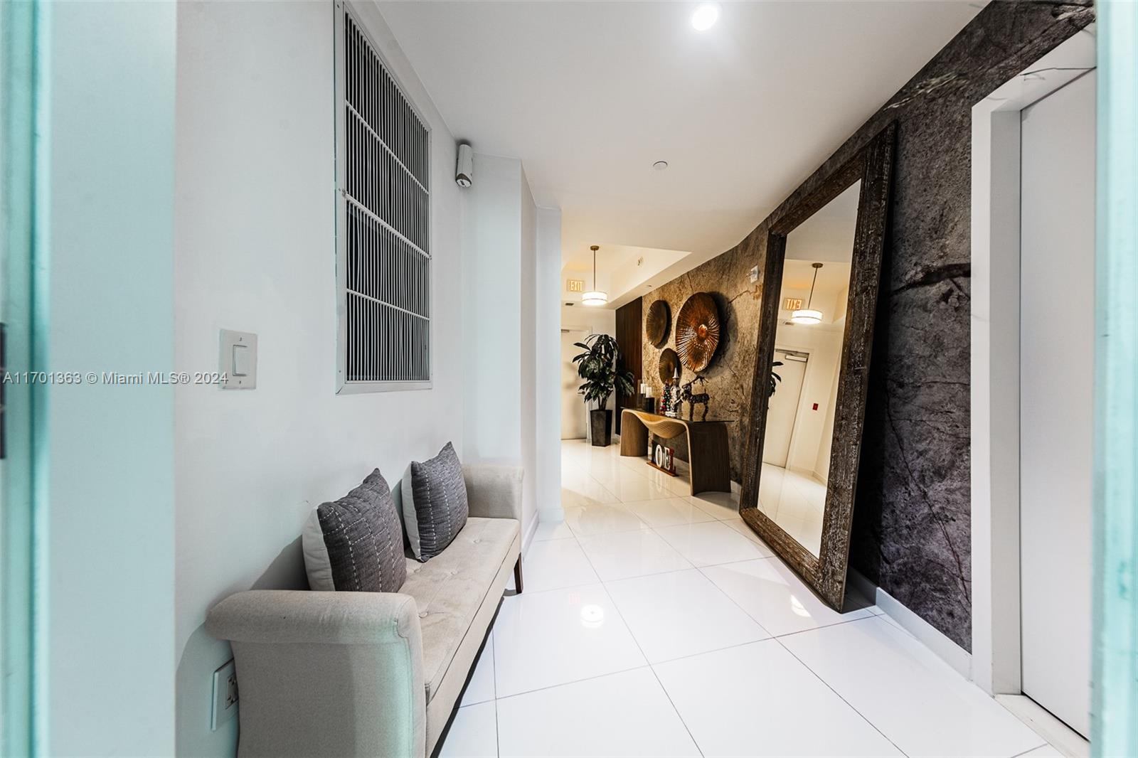 A modern hallway features white tile floors, a beige bench, and a large floor mirror — 851 NE 1st Ave # 2111, Miami FL 33132, MIAMI, FL