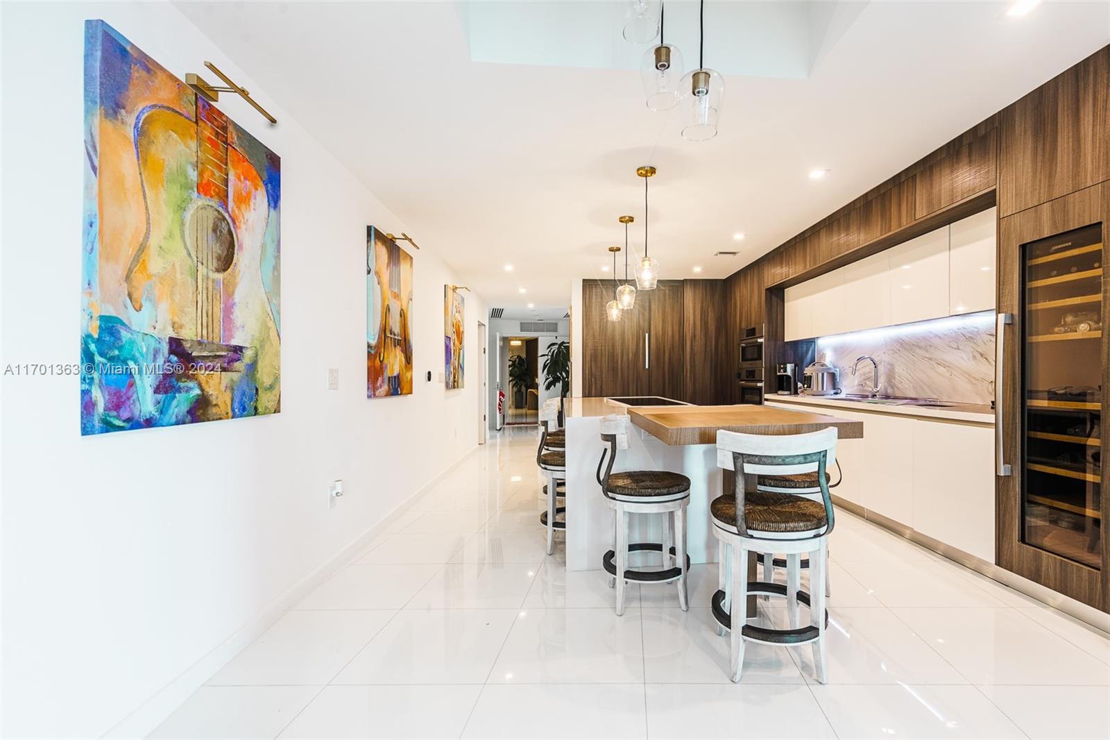 A modern kitchen features a central island with bar stools, white cabinetry, and colorful artwork — 851 NE 1st Ave # 2111, Miami FL 33132, MIAMI, FL