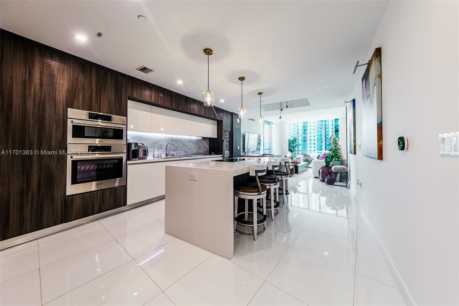 A modern kitchen features dark wood cabinetry, white countertops, an island, and glossy tile floors — 851 NE 1st Ave # 2111, Miami FL 33132, MIAMI, FL