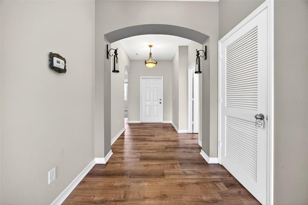 A hallway with wood-look flooring leads to a white door under an arched entryway — 24611 RIO VILLA LAKES CIRCLE, PUNTA GORDA, FL