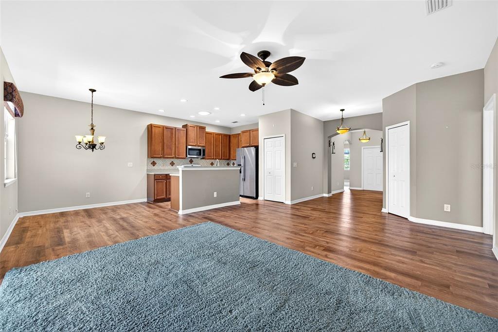 An open-concept living area features wood-look flooring, a blue area rug, and a kitchen — 24611 RIO VILLA LAKES CIRCLE, PUNTA GORDA, FL