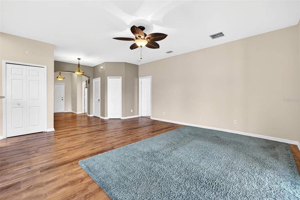 A living room features wood-look flooring, a large blue area rug, and a ceiling fan — 24611 RIO VILLA LAKES CIRCLE, PUNTA GORDA, FL