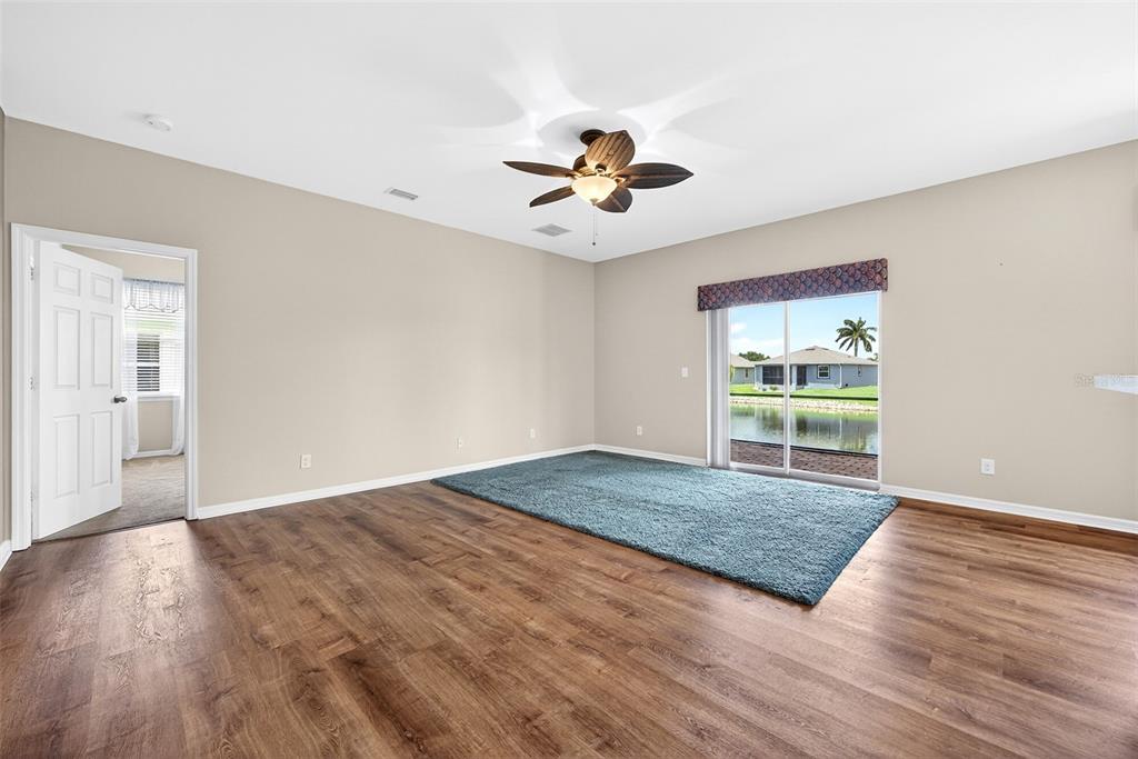 A room with wood-look flooring, a blue area rug, a ceiling fan, and sliding glass doors — 24611 RIO VILLA LAKES CIRCLE, PUNTA GORDA, FL
