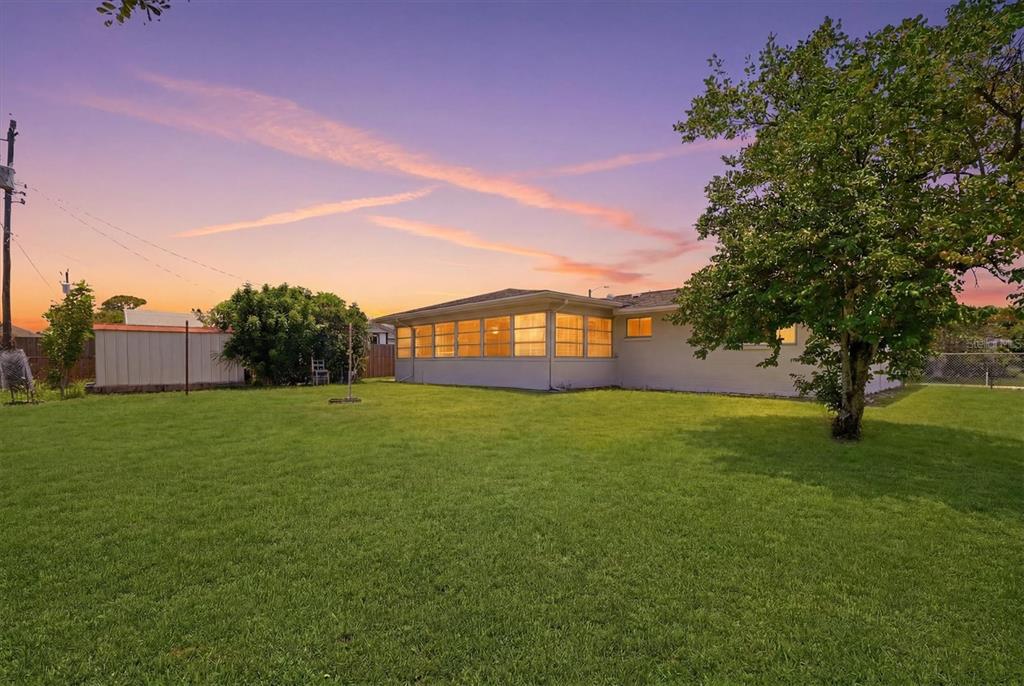 A backyard view of a single-story house with a large sunroom and a grassy lawn — 329 SAN BENITO AVENUE, NORTH PORT, FL
