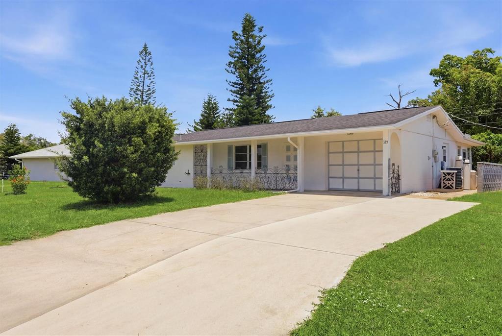 A white single-story house with a concrete driveway, a carport, and a large front bush — 329 SAN BENITO AVENUE, NORTH PORT, FL