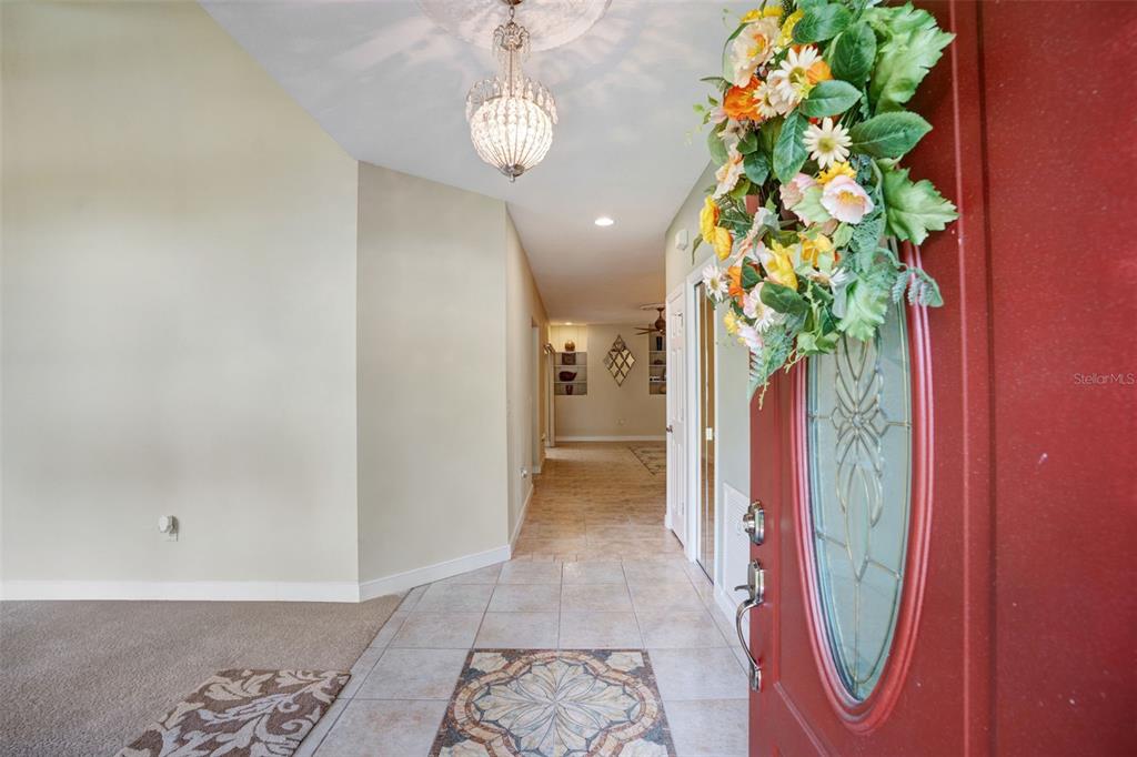 A view from an open red front door into a tiled foyer with a chandelier — 6253 MURIWOOD COURT, SARASOTA, FL