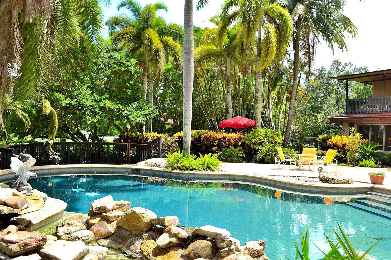 A swimming pool with a rock feature and patio area surrounded by lush tropical landscaping — 6200 SW 183rd Way, Southwest Ranches FL 33331, SOUTHWEST RANCHES, FL