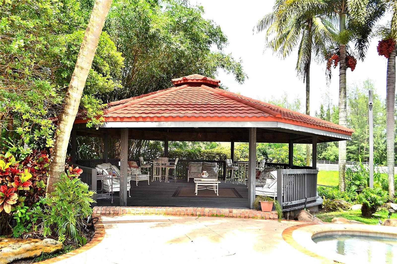 A covered outdoor gazebo with a tiled roof, wooden deck, and patio furniture near a pool — 6200 SW 183rd Way, Southwest Ranches FL 33331, SOUTHWEST RANCHES, FL