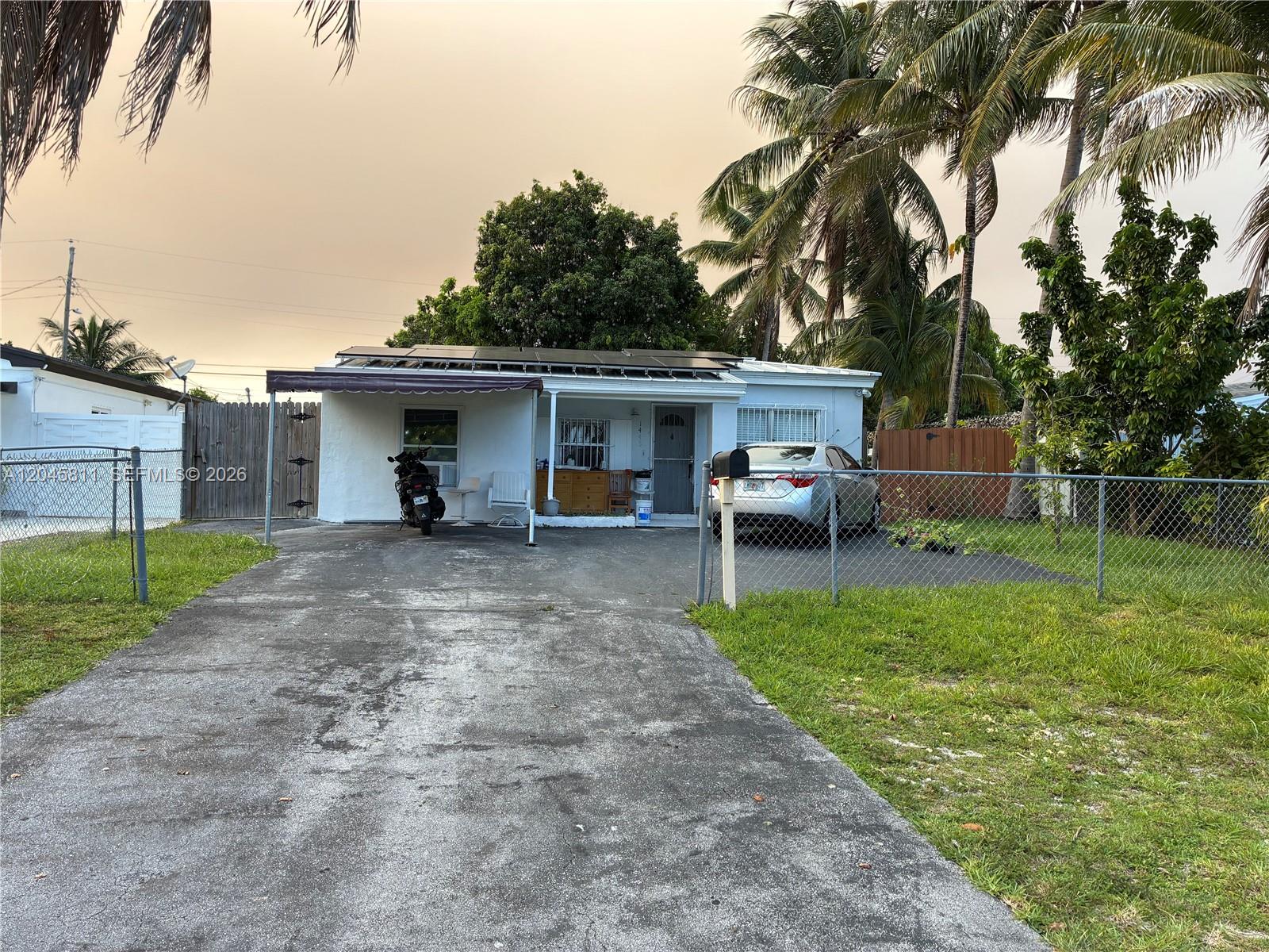 A single-story house with a concrete driveway, solar panels, and a chain-link fence — 1445 NE 174th St, North Miami Beach FL 33162, NORTH MIAMI BEACH, FL