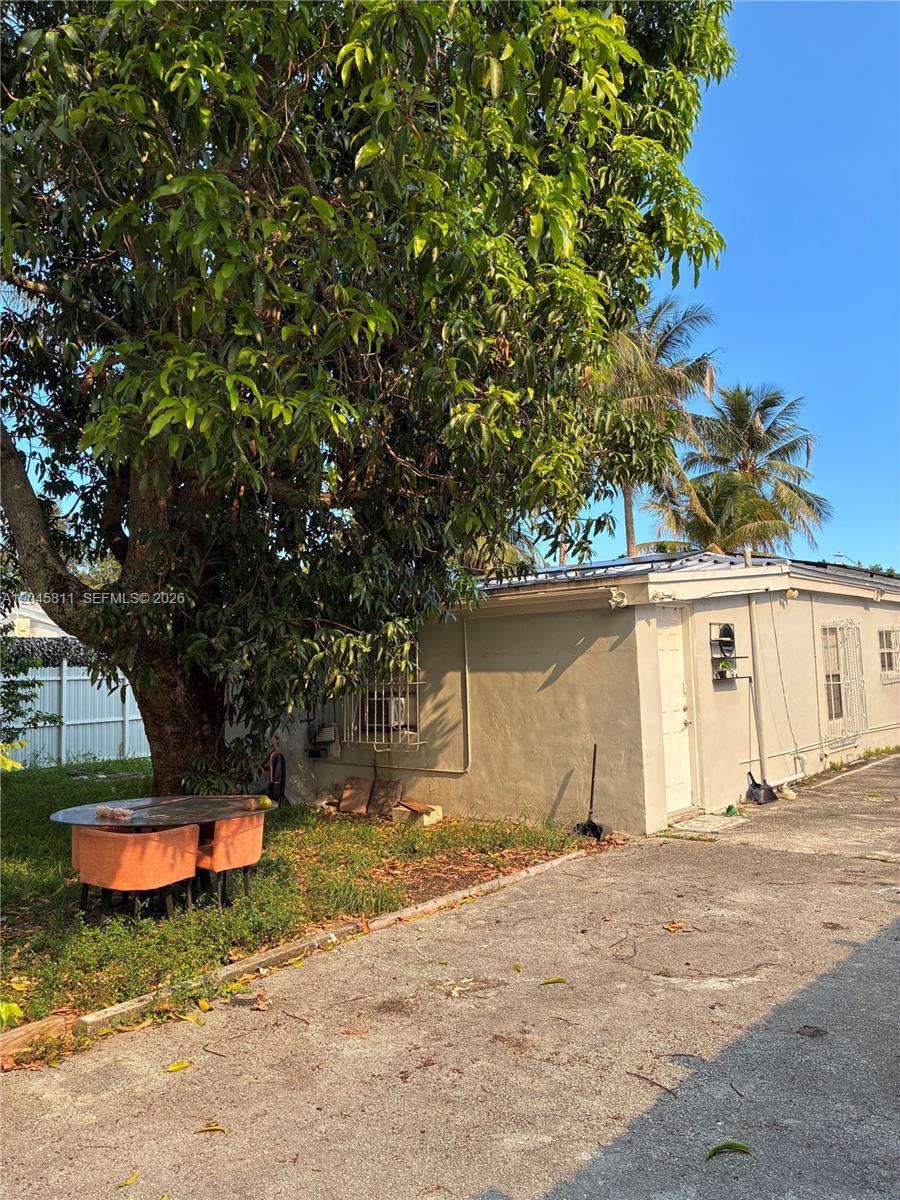 A large tree shades a small patio table and chairs next to a beige building — 1445 NE 174th St, North Miami Beach FL 33162, NORTH MIAMI BEACH, FL