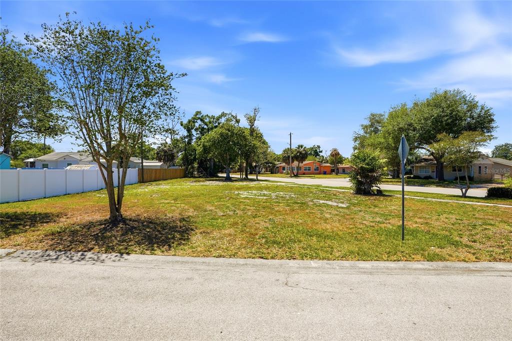 A vacant, grassy residential lot with trees and a white fence under a blue sky — 4716 IRIS STREET N, ST PETERSBURG, FL