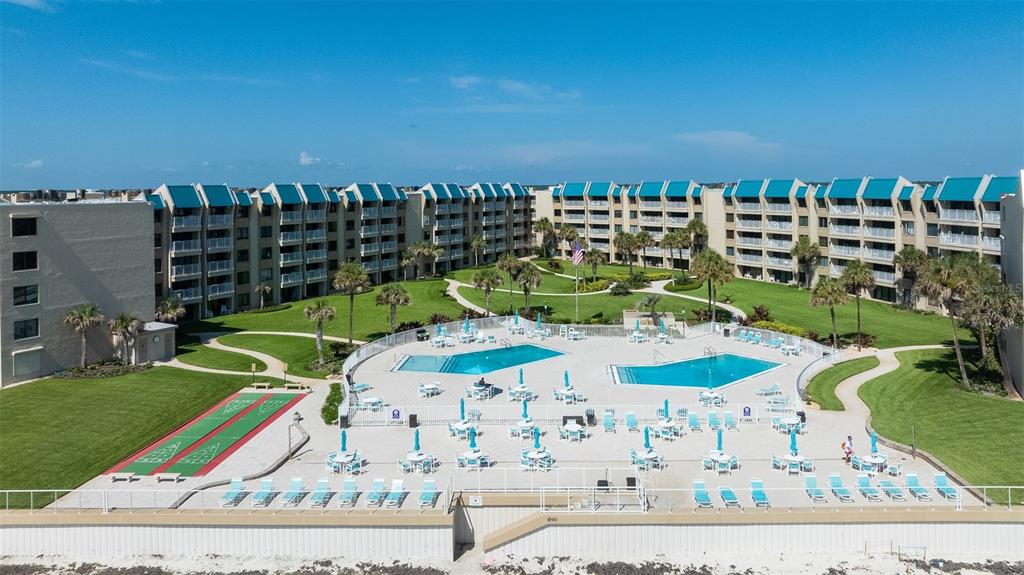An aerial view shows a multi-story resort building with two swimming pools and shuffleboard courts — 4501 S ATLANTIC AVENUE UNIT 5090, NEW SMYRNA BEACH, FL